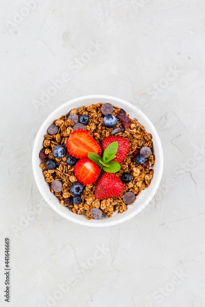Fototapeta Bowl of chocolate granola with blueberries and strawberry on grey top view. Healthy breakfast. Flat lay minimalist design. Space for text.