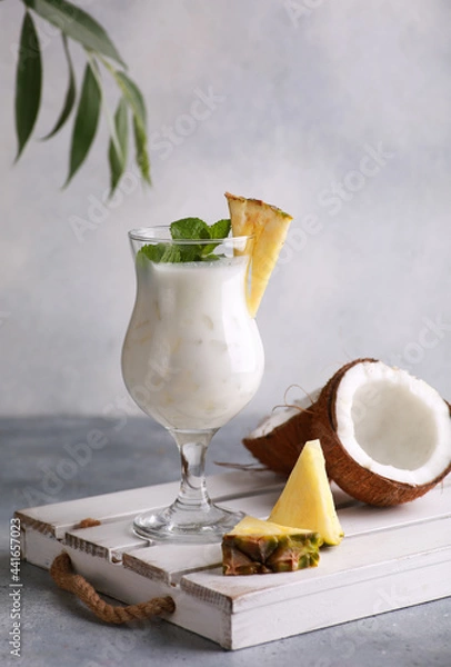 Fototapeta Summer. Drinks and cocktails. Pina colada in glass with pineapple, coconut, mint and a branch of greenery on a light gray background. Background image, copy space