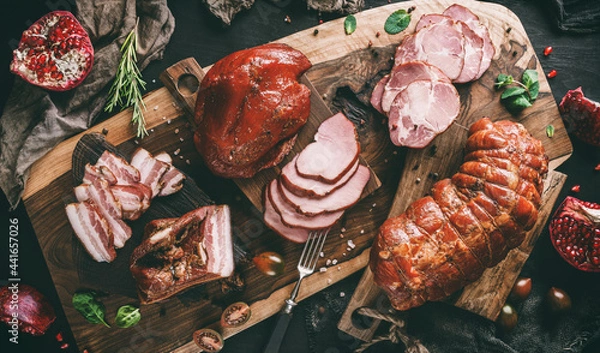 Fototapeta Assortment of cold meats products, ham, sausage, salami, parma, prosciutto, bacon on wooden cutting board with herb and spices over dark background. Meat appetizer, set of wine, top view, toning