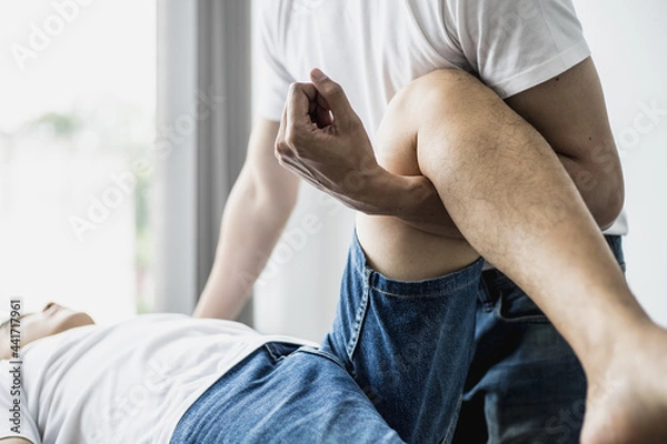 Fototapeta A professional physiotherapist is stretching the patient's legs, the patient has muscle dysfunction due to hard work, most often an office worker who has problems sitting for long periods of time.