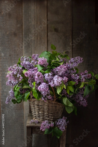 Fototapeta Bouquet of lilacs in a vintage basket. Beautiful violet Lilac flower still life Easter border design on wooden table.