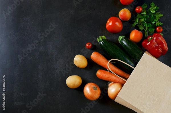 Fototapeta Shopping or delivery healthy food concept. Food supermarket and clean vegan eating concept. Fresh vegetables and fruits: carrot, potato, zucchini, tomato in paper bag on black background. Copy space.