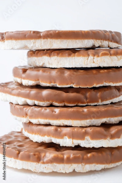 Fototapeta Pile of rice crispbreads coated with chocolate on white background close-up. Crispy puffed round rice bread for healthy diet.
