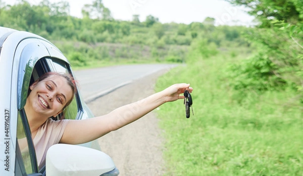 Fototapeta Young happy woman is sitting in the car, holding the keys in her hand. The girl is happy with the purchase, obtaining a driving license