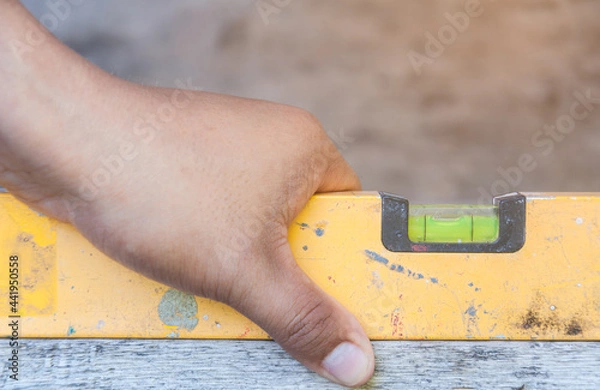 Fototapeta Mechanic's hand using water level meter measuring the wooden floor