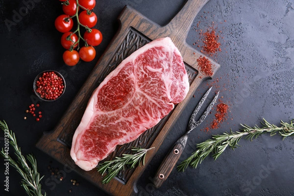 Fototapeta Raw meat steak. Japanese marble wagyu meat on a dark wooden board with spices, rosemary and fresh cherry tomatoes. Background image, copy space. Top view, flatlay
