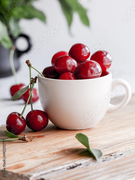 Obraz Fresh ripe cherries in white cup on wooden background
