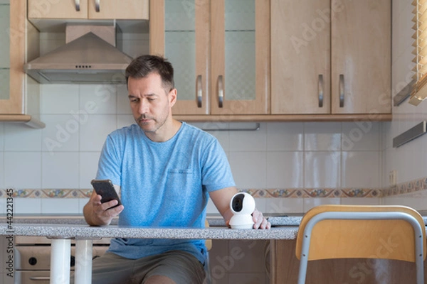 Fototapeta Man setting up security camera with his smartphone.