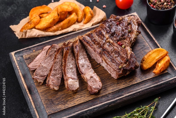 Fototapeta Delicious juicy fresh beef steak with spices and herbs on a dark concrete background