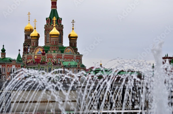 Fototapeta The Cathedral of the Epiphany in the foreground of the fountain jet is cloudy weather. Russia Yoshkar-Ola 01.05.2021. High quality photo