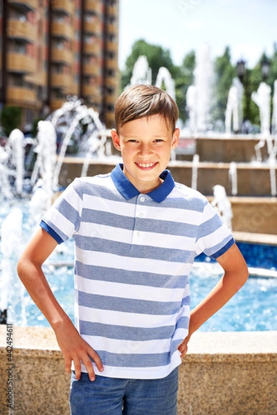 Fototapeta a beautiful boy on vacation in the summer in the city near the fountain