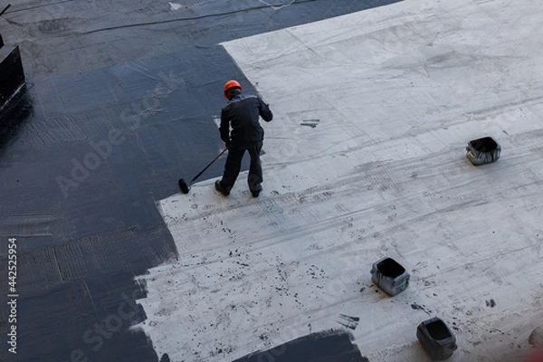 Fototapeta Waterproofing coating. A worker applies bitumen mastic to the foundation. Roofer cover the waterproofing primer on the roof, modified with polymer bitumen, with a roller brush.