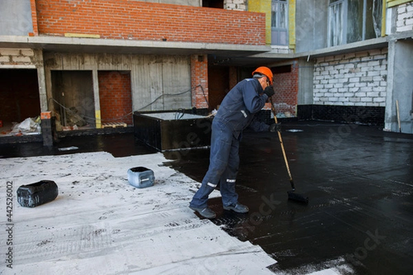 Fototapeta Waterproofing coating. A worker applies bitumen mastic to the foundation. Roofer cover the waterproofing primer on the roof, modified with polymer bitumen, with a roller brush.