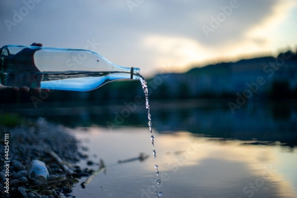 Fototapeta Glasflasche giesst Wasser in den Fluss