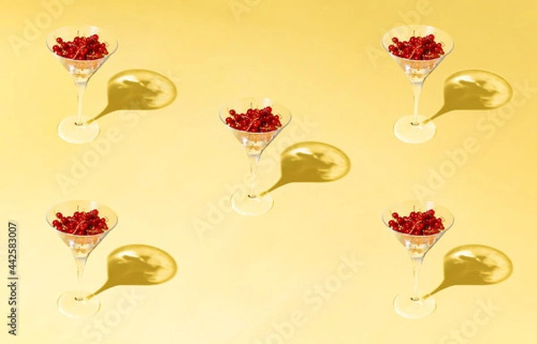Fototapeta Creative summer pattern made of martini glasses filled with red fruit against yellow sunlit background. Minimal party lay out.