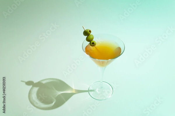 Obraz Martini glass filled with orange drink and olives on stick against turquoise sunny background. Minimal summer refreshment concept.