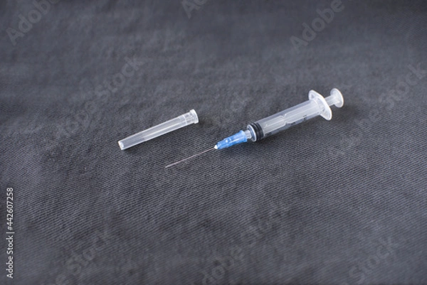 Fototapeta a disassembled medical syringe for injection with a metal needle lies on a dark gray fabric background