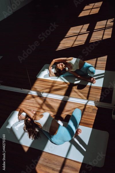 Fototapeta Young fit woman do stretching exercises in front of a mirror on a mat in a bright sunny classroom