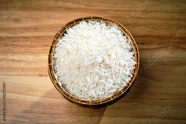 Fototapeta overhead flat lay shot of raw Thai's jasmine rice in Thai's traditional style bamboo's bowl on wooden dinner table with light and shade