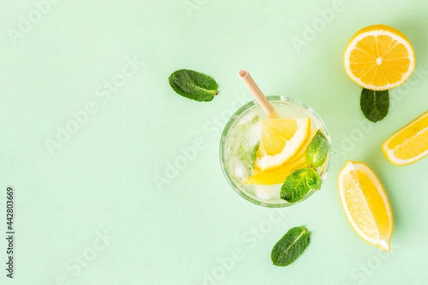 Fototapeta Ice lemon water or lemonade with mint on a green background. A glass of fresh fruit drink for summer heat.