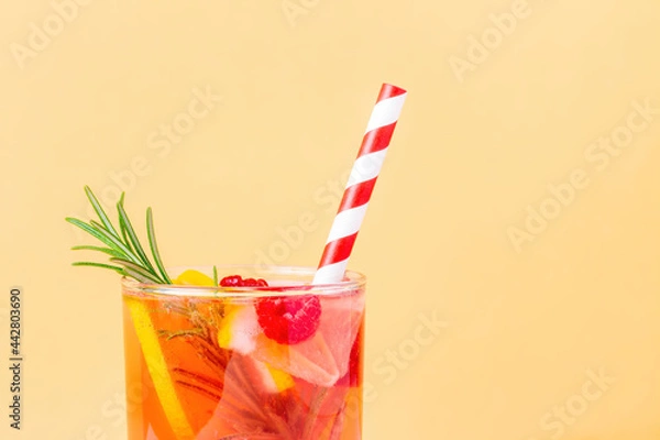 Fototapeta Nonalcoholic cocktail with lemon and raspberry and rosemary on a beige background. Top of glass with lemonade and striped disposable straw for summer heat.