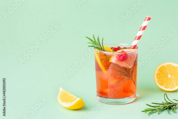 Fototapeta Fresh red water with lemon and raspberry and rosemary on green background. Exotic summer drink with citrus slices with copy space.