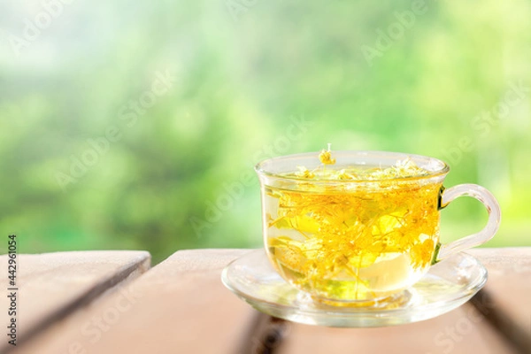 Fototapeta Herbal tea from linden flowers in a cup on a wooden table against the background of nature. 
