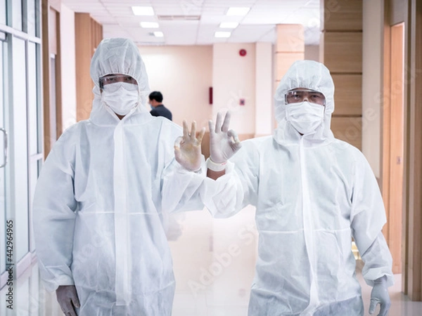 Fototapeta Medical workers in plague suits raise their hands to mark OK while on duty related to coronavirus.