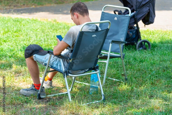 Fototapeta A guy with a phone in nature in an armchair.