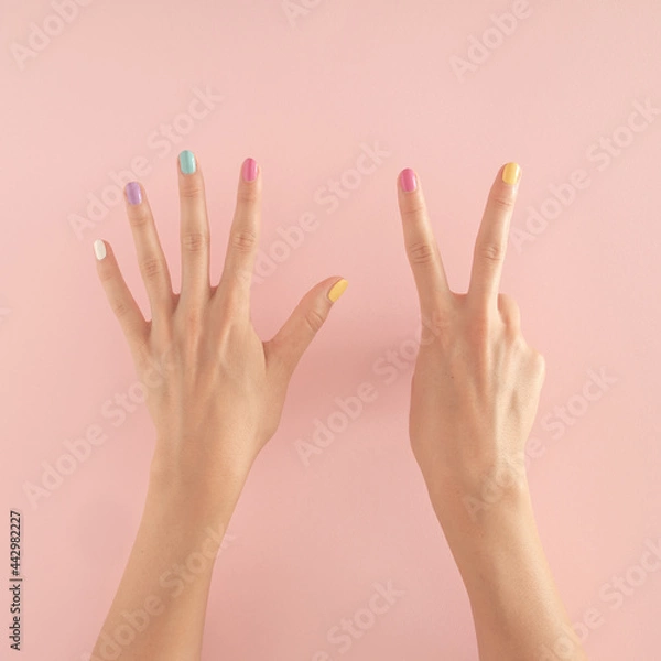 Fototapeta women hands with colorful nails on the pastel pink background. copy space.  summer modern tropical abstract art with female hand. minimal background idea with number seven