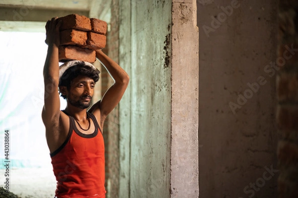 Fototapeta A DAILY WAGE LABOURER CARRYING BRICKS ON HEAD FOR CONSTRUCTION