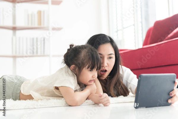 Obraz Happy Asian young mother and daughter playing tablet together in living room on holiday