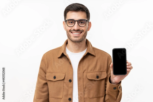 Fototapeta Young smiling man in casual shirt showing blank screen smartphone in hand, isolated on gray background