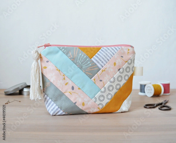 Fototapeta Patchwork zipper pouch with tassel zipper pool, thread spools, little scissors and pins in metal jar on wooden desk over white