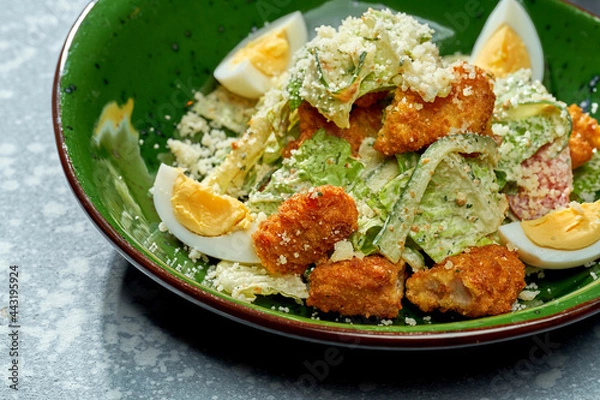 Fototapeta Appetizing salad with chicken breaded and deep fried, parmesan, egg, lettuce and white sauce in a green plate on a blue background