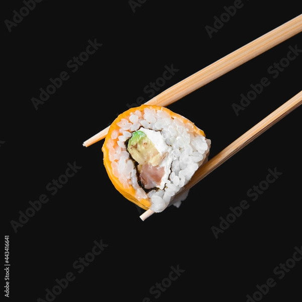Fototapeta One piece of sushi in chopsticks, isolated on black background. Japanese cuisine concept, copy space banner.