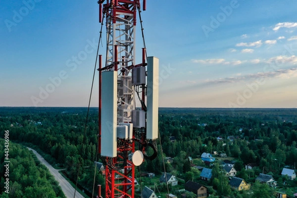 Obraz A cell tower against a blue sky and woodland, shooting from a drone.