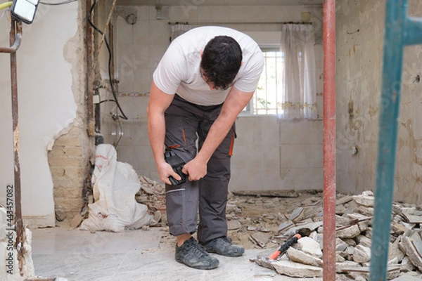 Fototapeta Young builder wearing knee protection pads to work in a construction. Safety at work.
