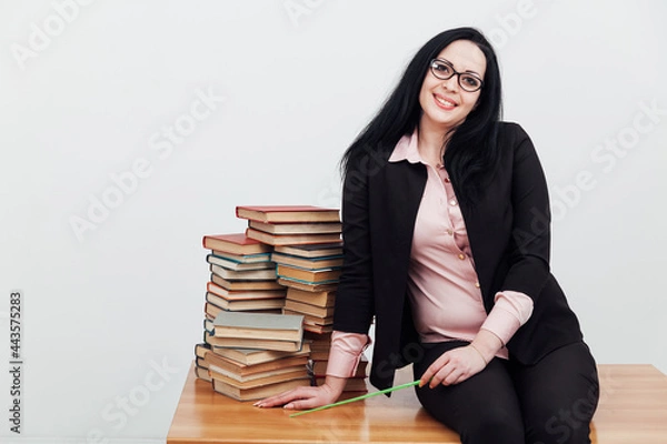 Fototapeta beautiful female teacher in class at a table with stacks of educational books