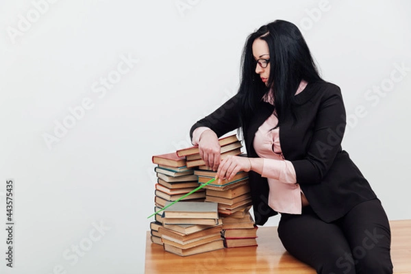 Fototapeta beautiful female teacher in class at a table with stacks of educational books