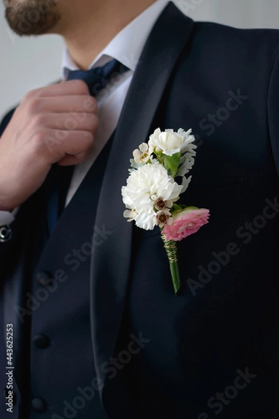 Fototapeta Groom in a dark blue suit with a boutonniere adjusts his tie looking to the side in close-up