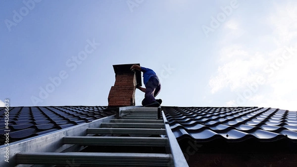 Obraz a chimney sweep climbs a metal ladder to the roof of the bathhouse to clean the pipe from burning