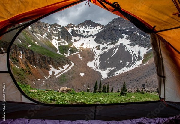 Fototapeta View of a mountain peak with snow on it through an orange camping tent at Blue lakes in Colorado. 
