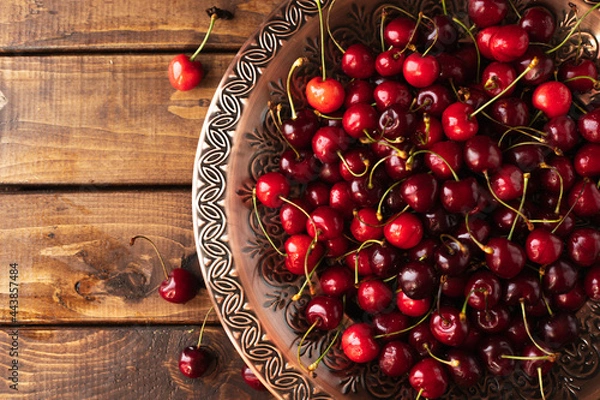 Fototapeta a lot of ripe cherries are lying on a copper tray with a pattern.