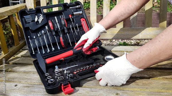 Obraz the hands of a man in work gloves open a suitcase with various tools. to work, you will need a screwdriver, keys, a tape measure