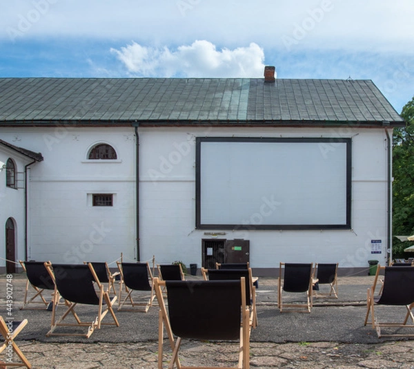Fototapeta Oper-air, outdoor cinema in the yard of brewery in Zwierzyniec, Poland. Rows of simple, black sunbeds in front of screen installed on the wall.