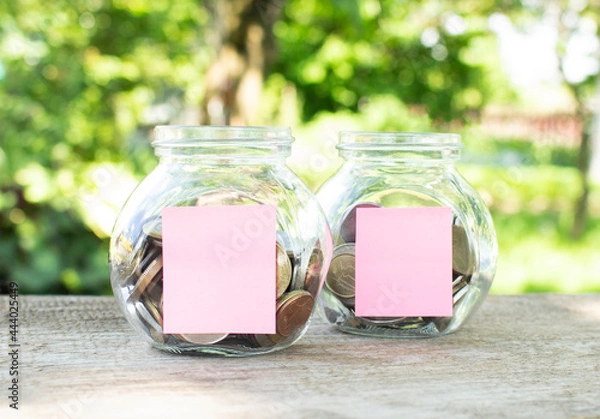 Fototapeta On a wooden table, there are glass jars with coins and attached blank stickers for inscriptions. Investment budget.