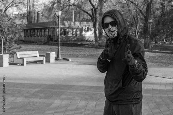 Fototapeta The man in a black suit and mask stands in a menacing pose. The criminal threatens with fingers in the form of pistols. Funny threat.
