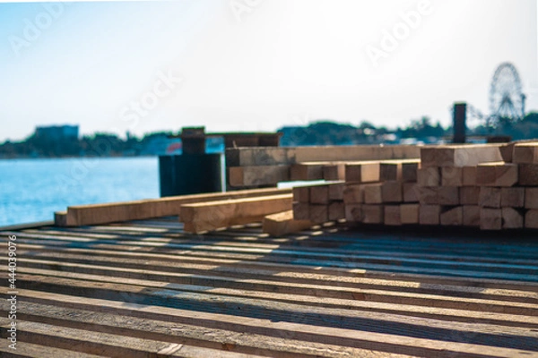 Fototapeta Piled wood on a pier under construction. Tree for building in the sunlight on a background of blue sea. Building a pier in the morning light of the sun.