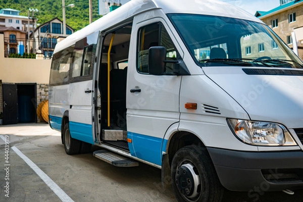 Fototapeta Tourist minibus is waiting with the door open in the parking lot. White minibus is parked in sunny weather.